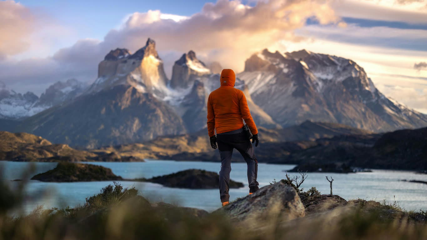 Hiker in an orange jacket overlooking a mountain lake at dusk